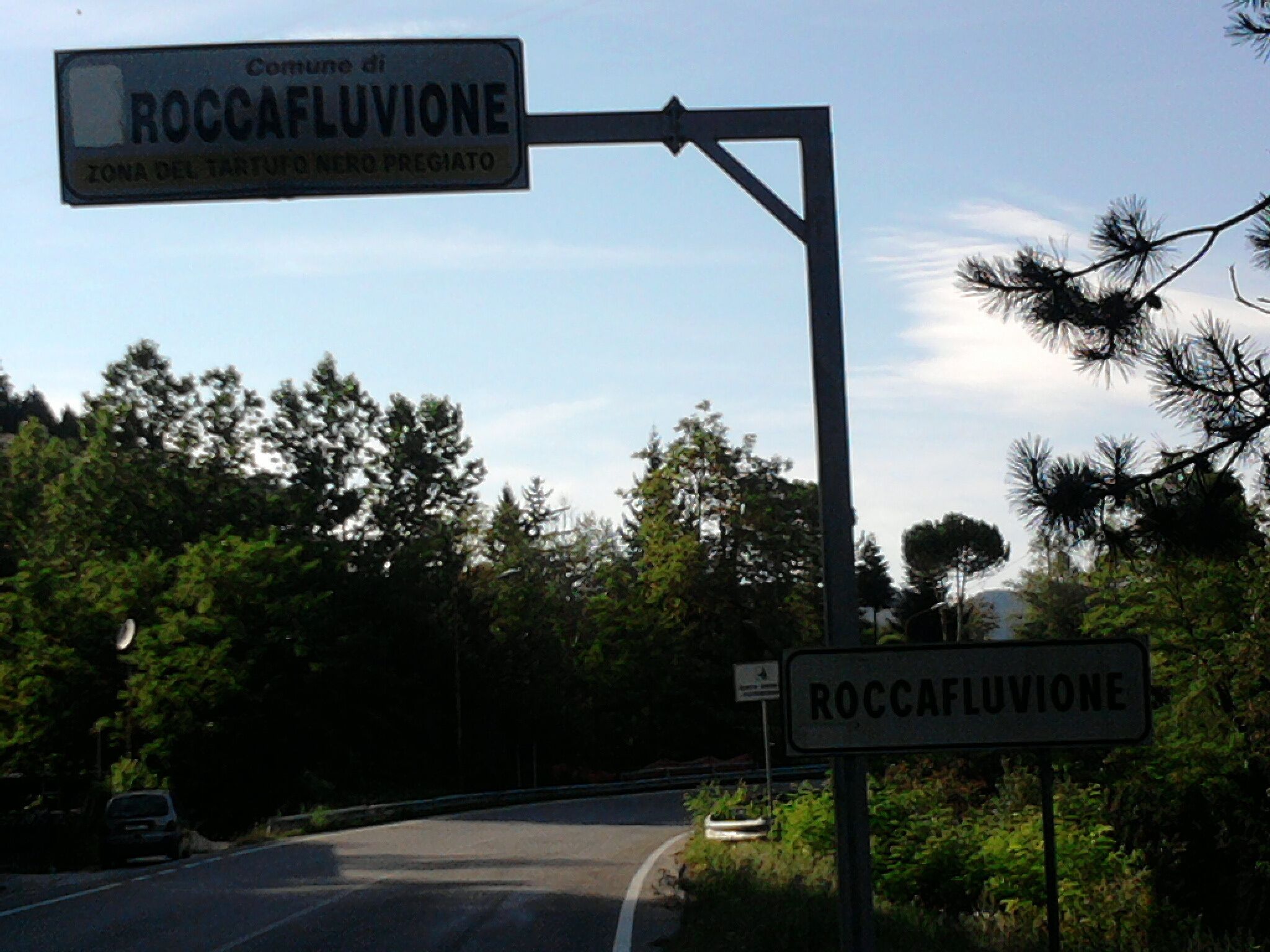 A road sign for Roccafluvione with a clear sky and trees in the background.