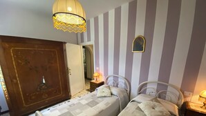 Ein Zimmer mit zwei Betten, einem Holzschrank, einer Kandelaberleuchte und einer gestreiften Wand.