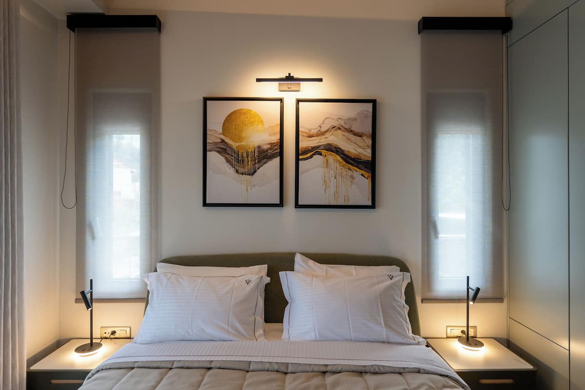 A modern bedroom with a bed, two bedside tables, a nightstand, a wall-mounted light, and two framed artworks above the bed.