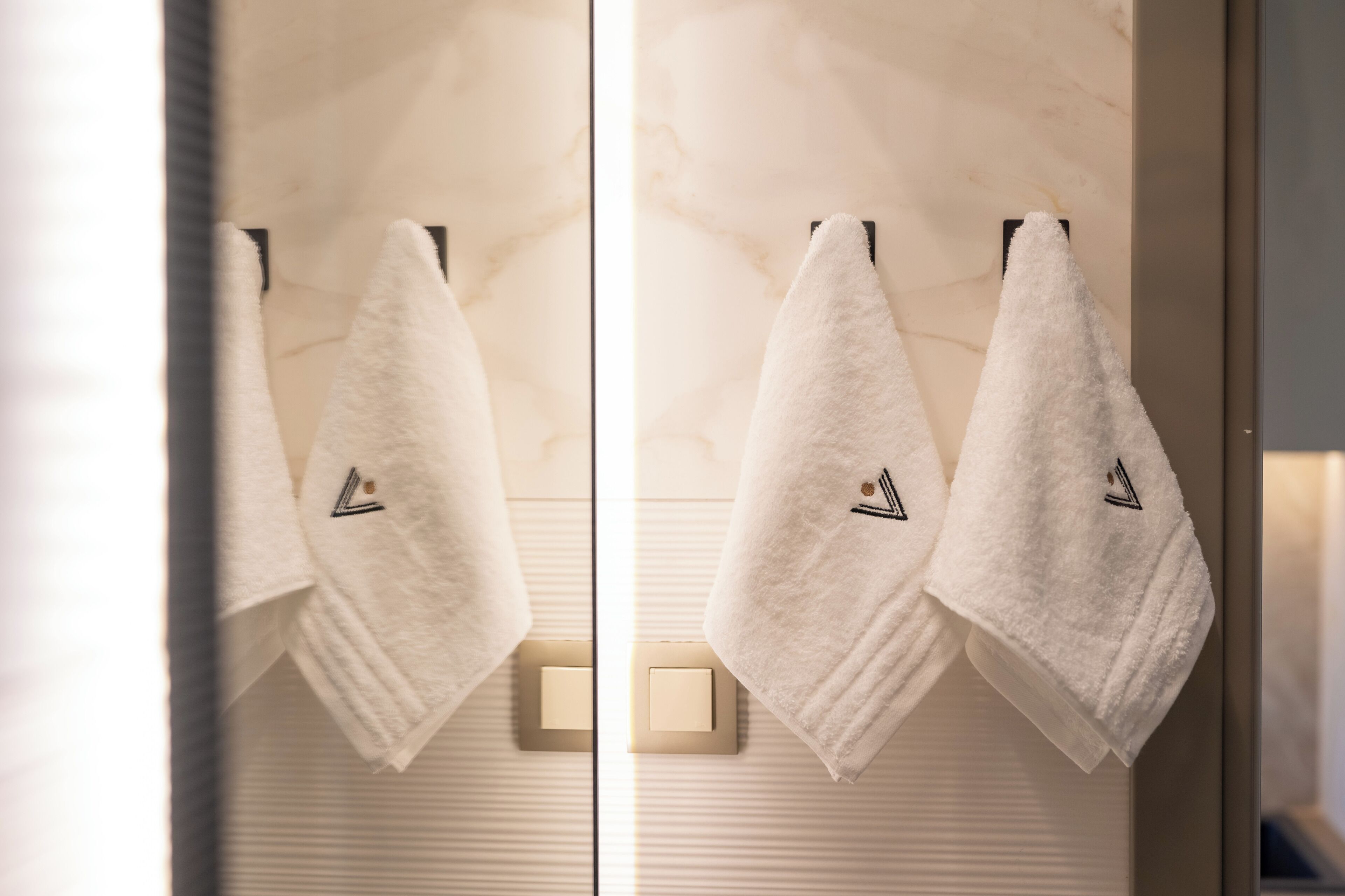 Two white towels hanging on a wall-mounted towel rack in a bathroom with a marble-like texture.
