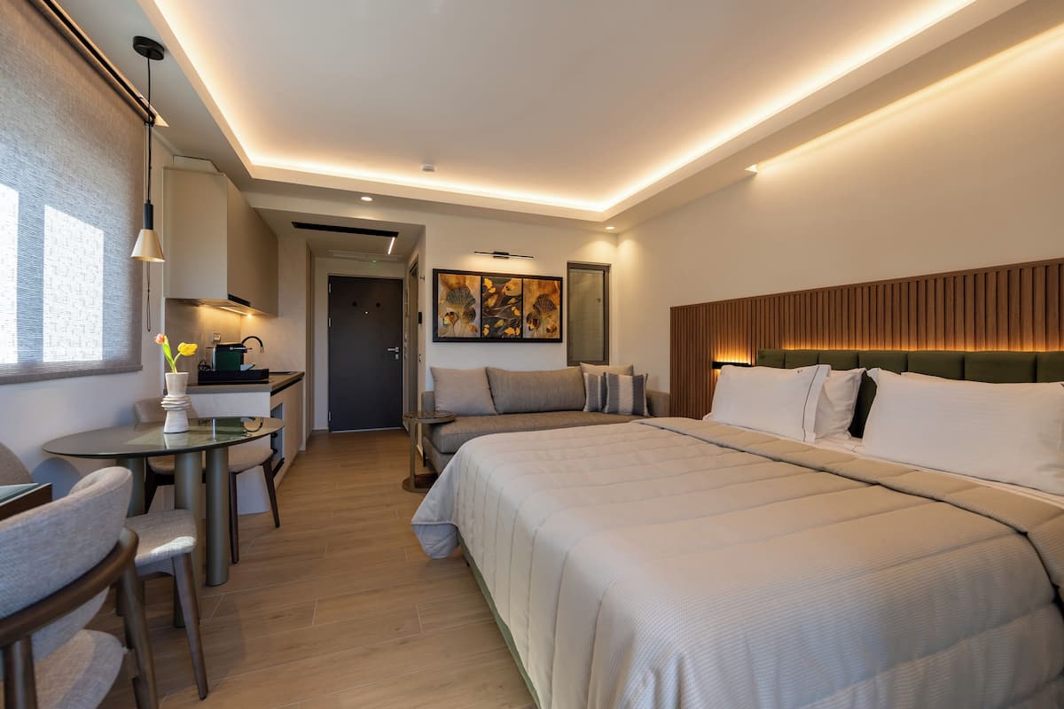 A hotel room with a bed, a desk, a chair, a small table, and a painting on the wall.