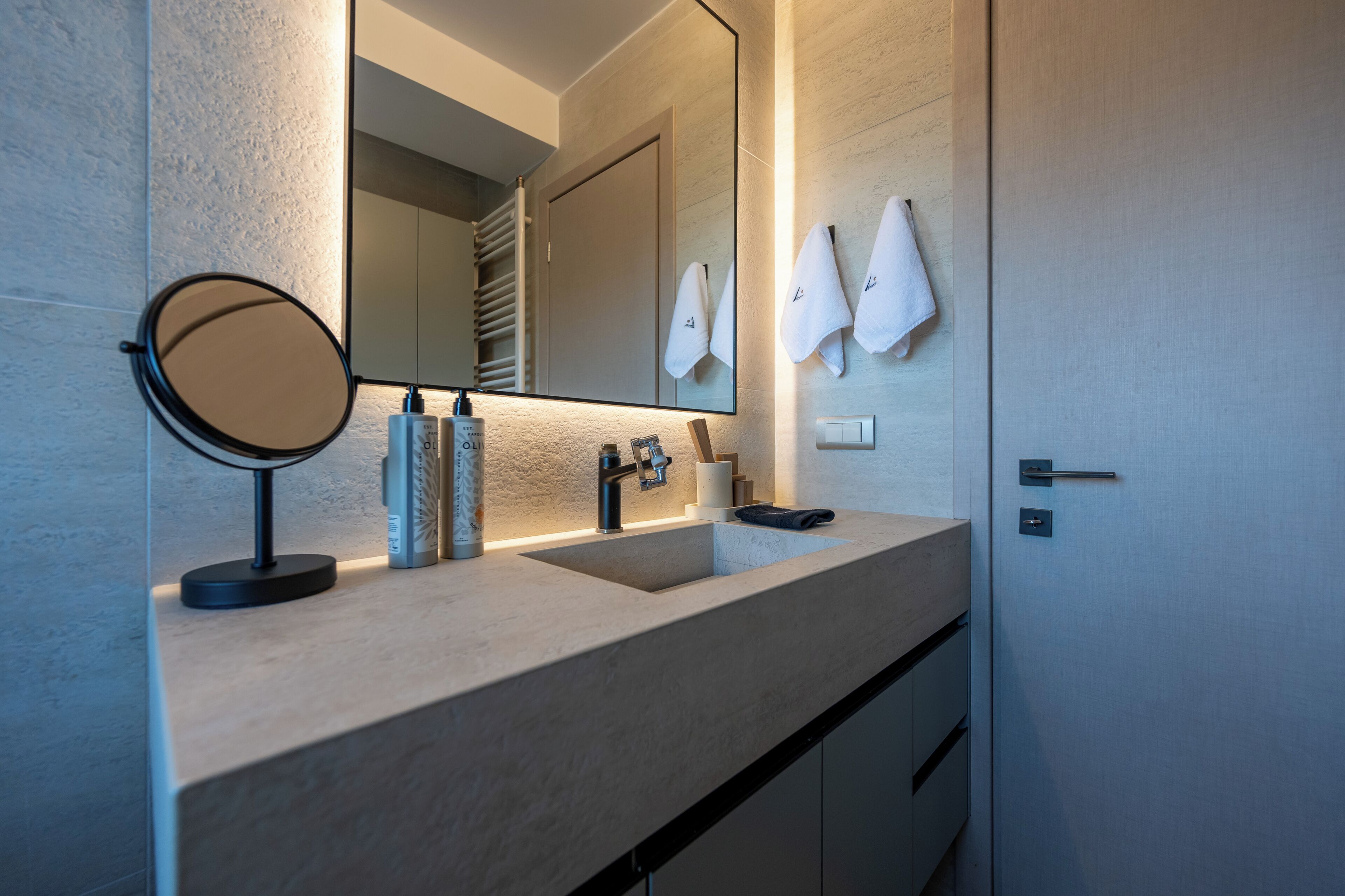 A modern bathroom with a large mirror, a sink, and two towels hanging on the wall.