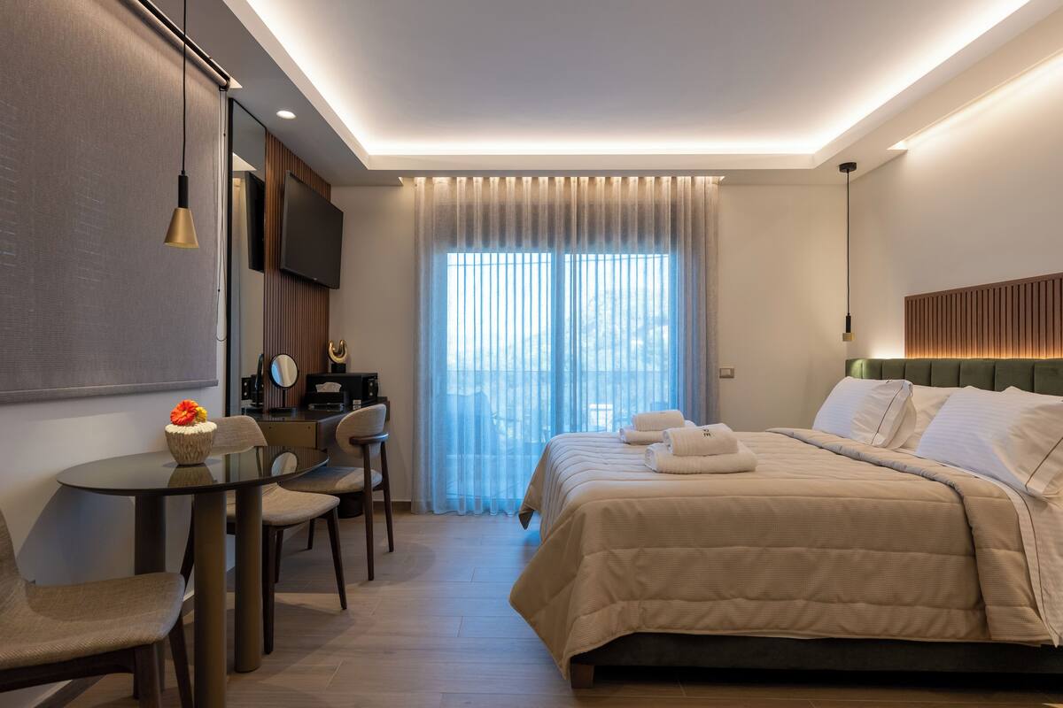 A modern hotel room with a bed, a desk, a chair, a TV, and a window with curtains.