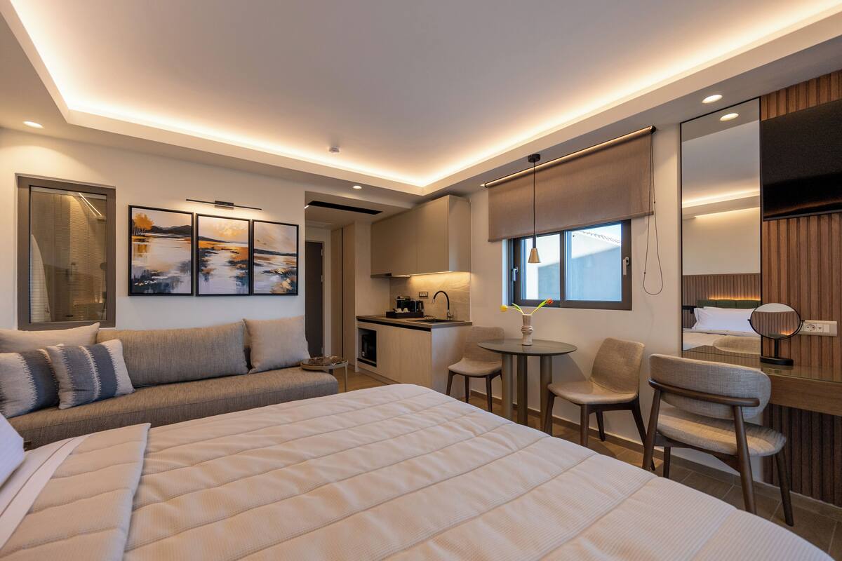A modern hotel room with a large bed, a sofa, a desk, and a dining area.