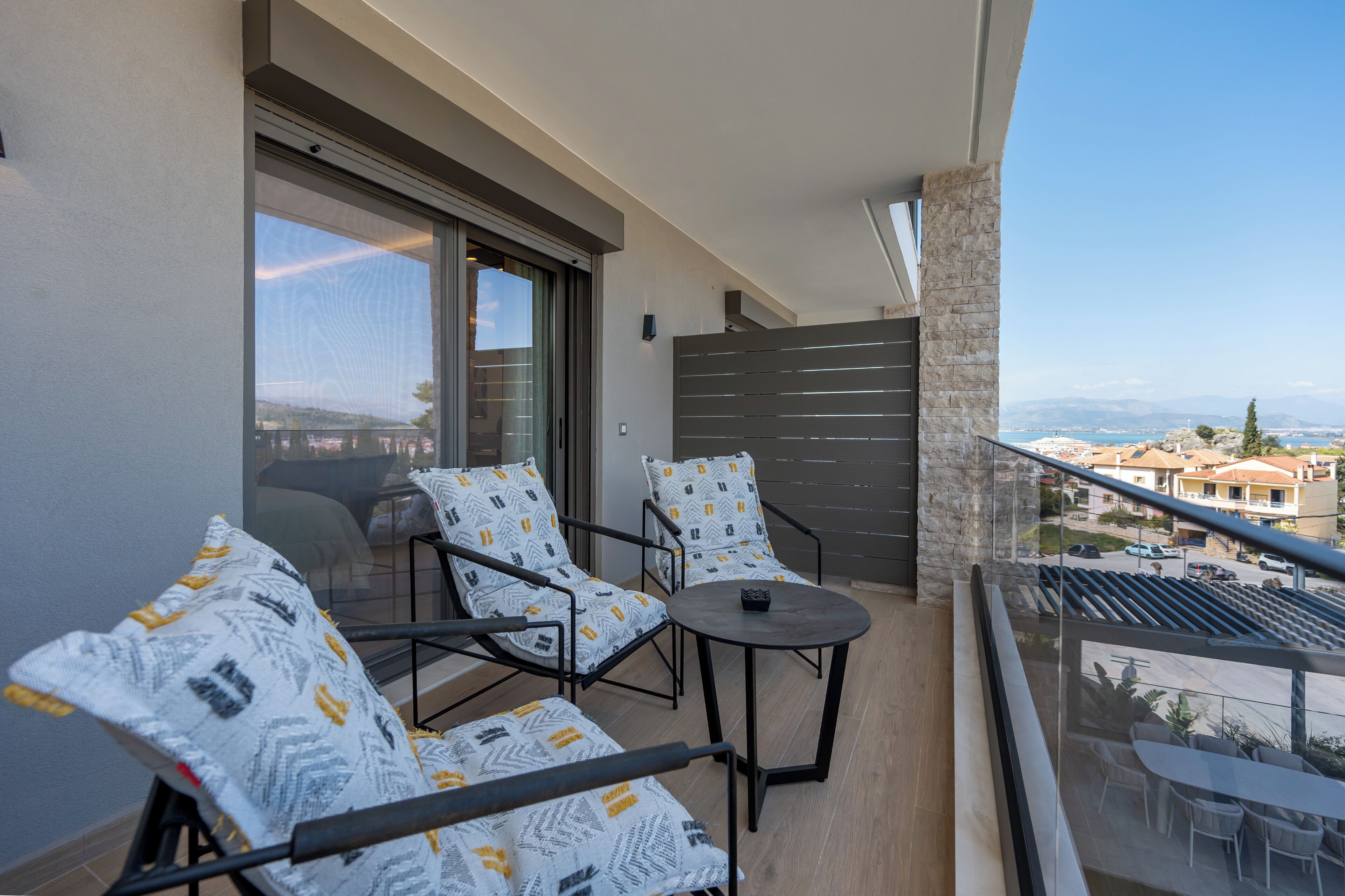 Un balcon avec deux chaises et une petite table, une vue sur la ville et un pilier en pierre.
