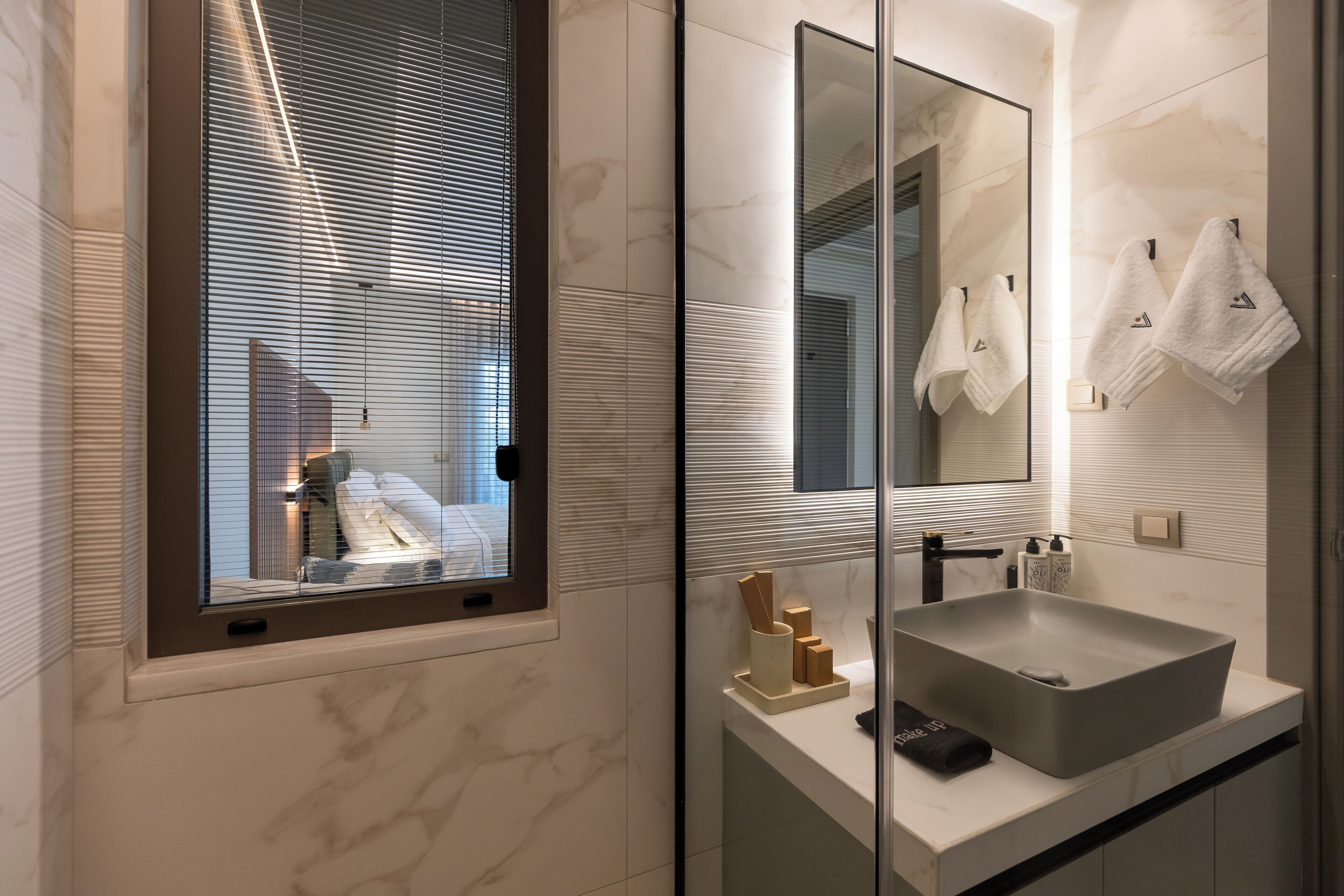 A modern bathroom with a large mirror, a rectangular sink, and a window with blinds.