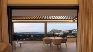 Une chambre moderne dotée d’une grande fenêtre, d’une table ronde avec des chaises et offrant une vue sur un paysage montagneux.