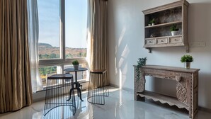 Una habitación con un ventanal grande, una consola de madera con plantas, una mesita redonda y dos sillas.