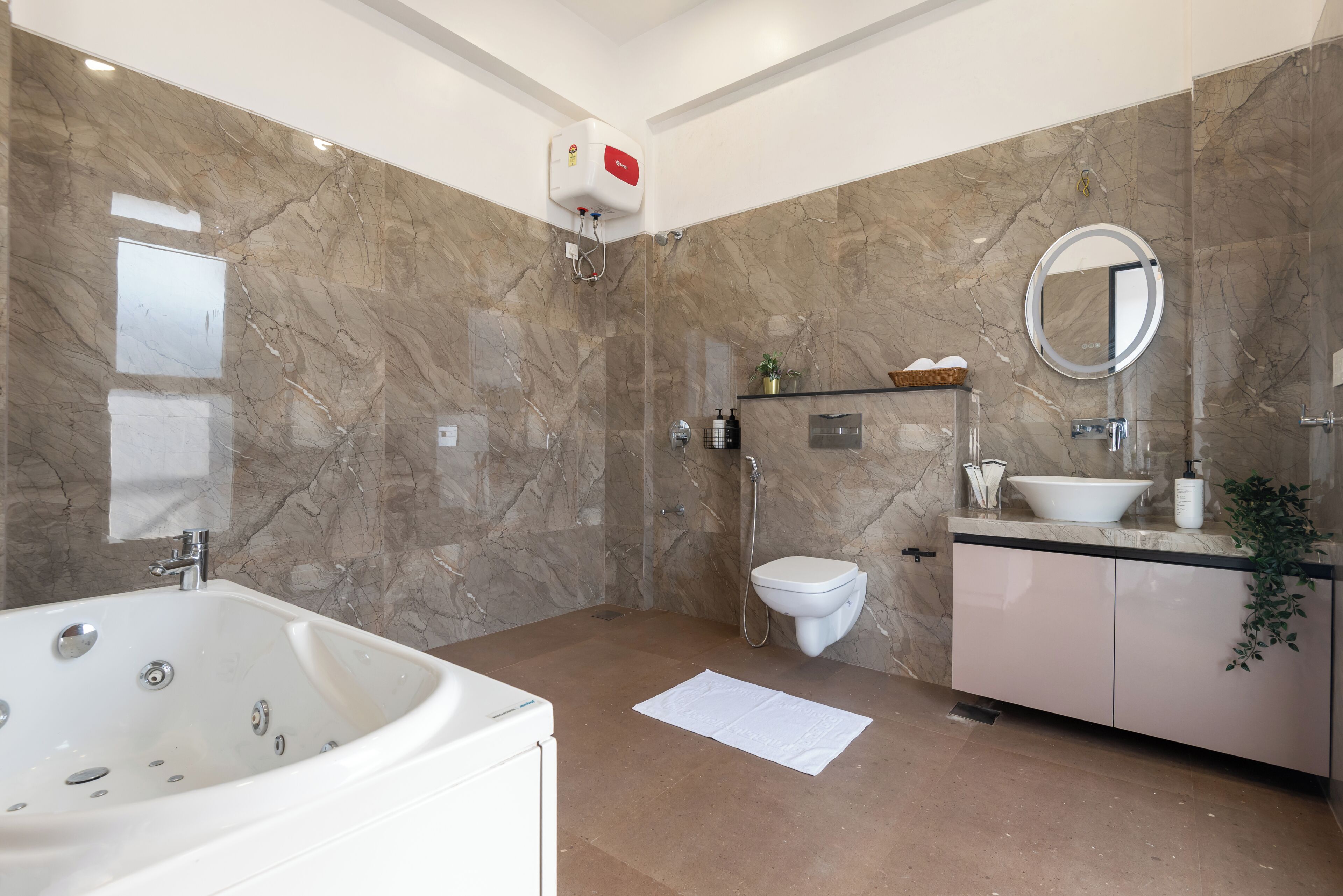 A modern bathroom with a bathtub, toilet, and sink, marble walls, and a ceiling-mounted showerhead.