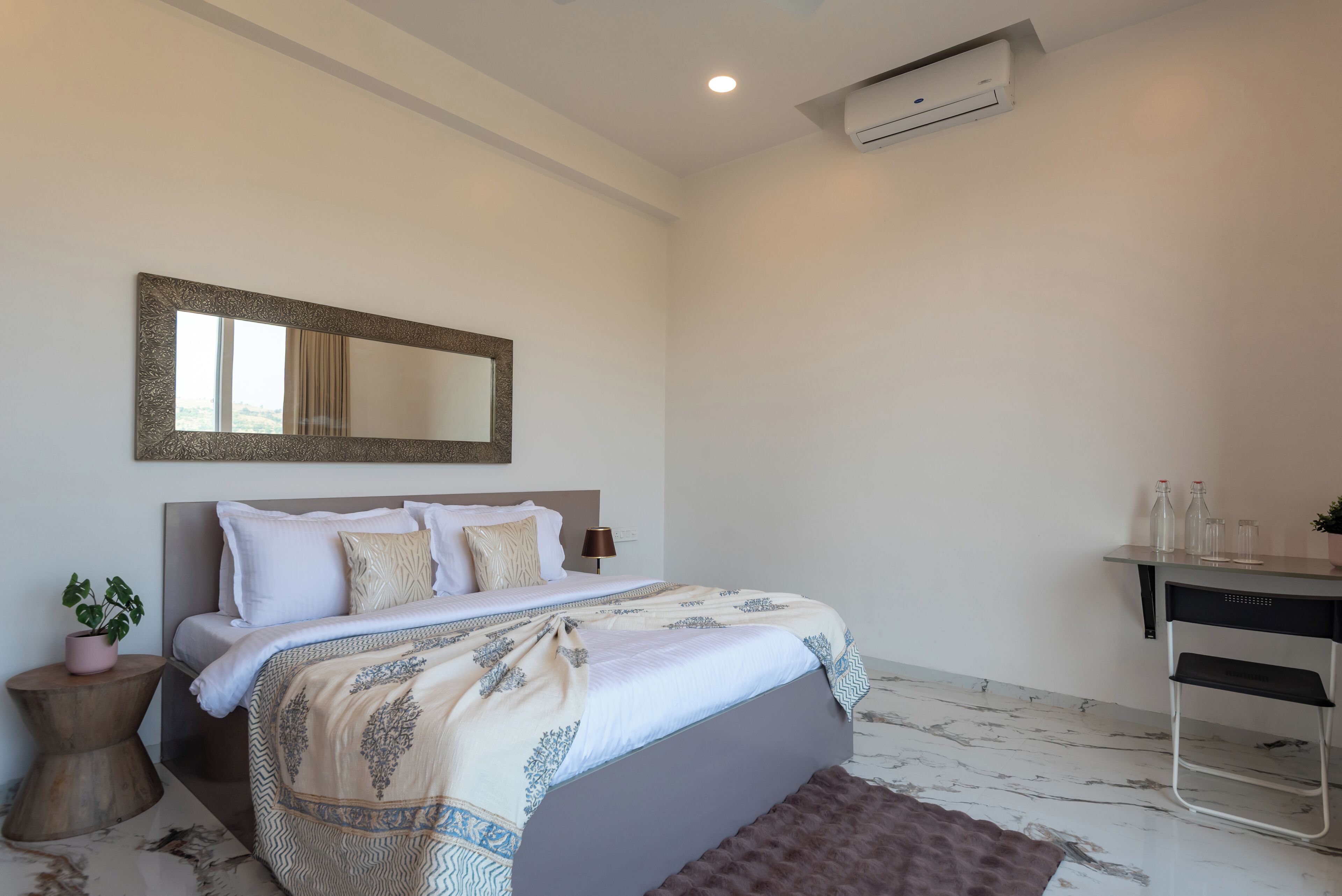 A bedroom with a bed, bedside table, lamp, and a desk with a chair.