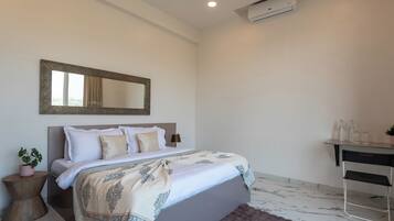 A bedroom with a bed, bedside table, lamp, and a desk with a chair.