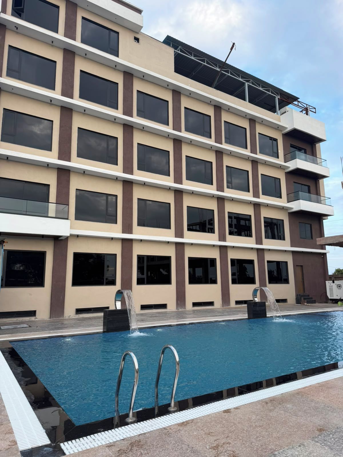 A multi-story hotel with a swimming pool, balconies, and a clear sky.