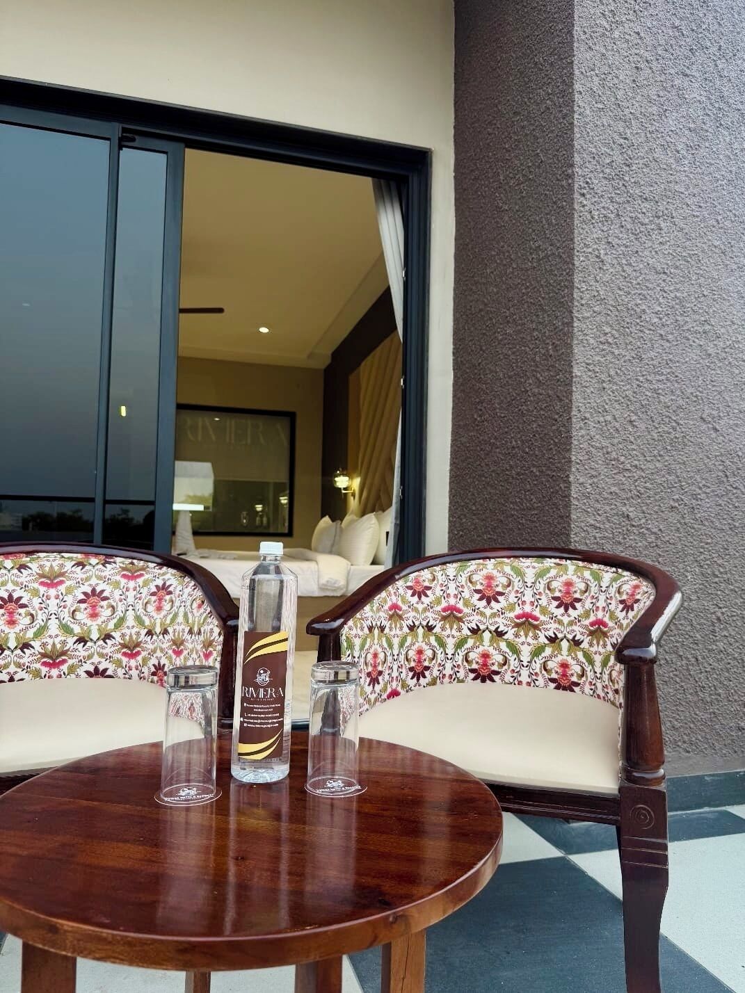 Une table en bois, deux chaises rembourrées, une bouteille de rhum et un verre.