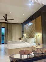 Habitación de hotel moderna con una cama grande, ventilador de techo, una mesa redonda y vistas al exterior.