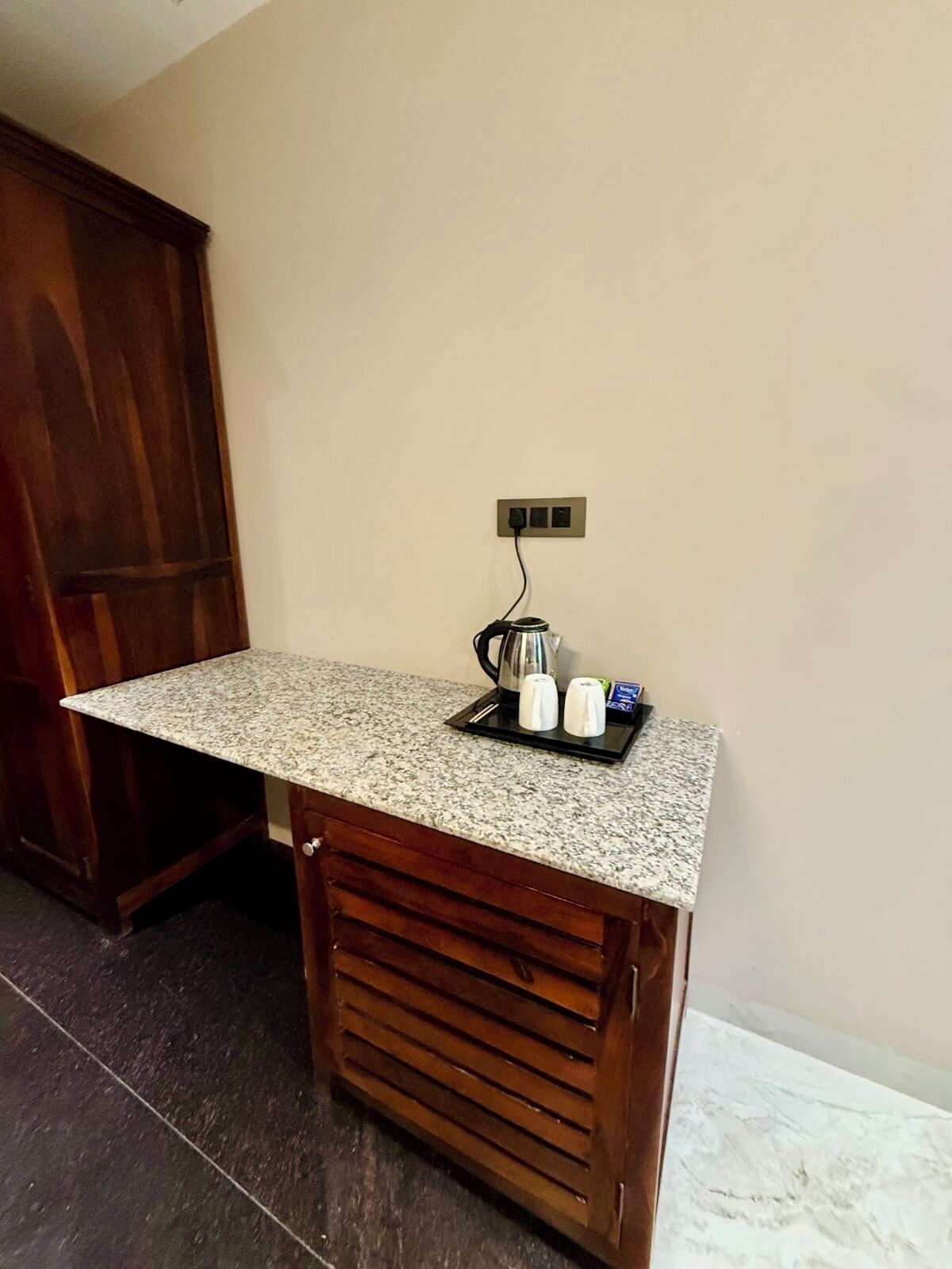 A kitchen area with a granite countertop, a coffee maker, salt and pepper shakers, and a power outlet on the wall.