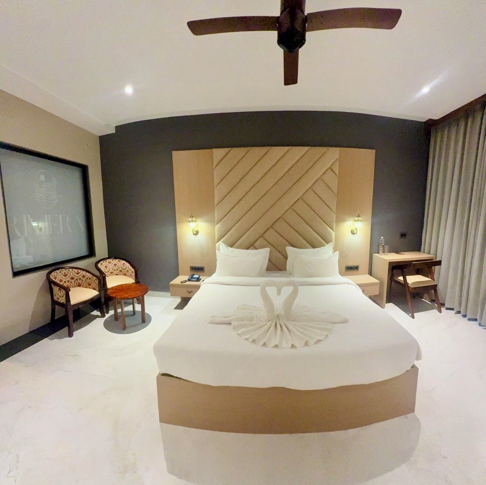 A modern hotel room with a large bed, a ceiling fan, a TV, and a desk with a chair.