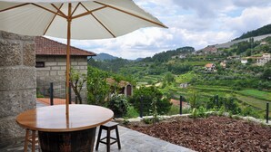 Une table avec un plateau en bois et un parasol blanc, donnant sur un vignoble avec des maisons situées sur une colline.
