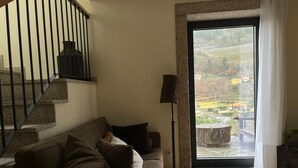 Un salon avec un escalier, un canapé, une lampe sur pied et une vue à travers une porte vitrée.