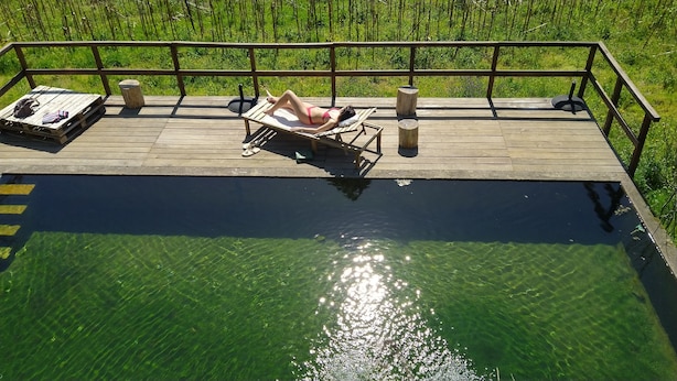 Une terrasse en bois avec une piscine, des chaises longues et une rambarde.