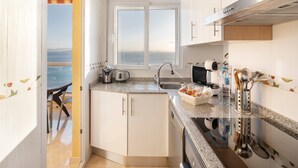 Une cuisine compacte avec vue sur la mer, un coin repas et un petit îlot central équipé d’appareils de cuisine.