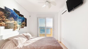 Une chambre avec un lit, un ventilateur de plafond, un téléviseur fixé au mur et une porte-fenêtre coulissante donnant sur un balcon.