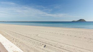 Une plage avec un ciel dégagé, un rivage sablonneux et une montagne qui se profile à l’horizon.