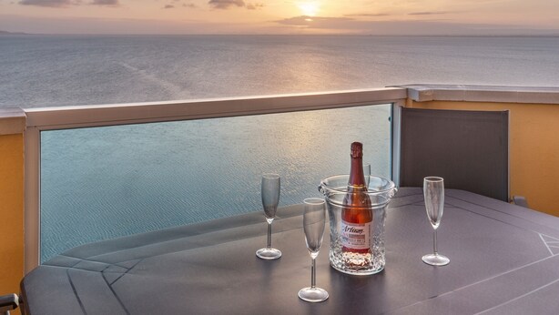 Une table avec une bouteille et des verres sur un balcon donnant sur la mer.