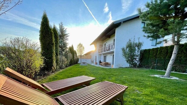 Een modern huis met een verzorgd gazon, twee houten ligstoelen en een helder uitzicht op de achtertuin.