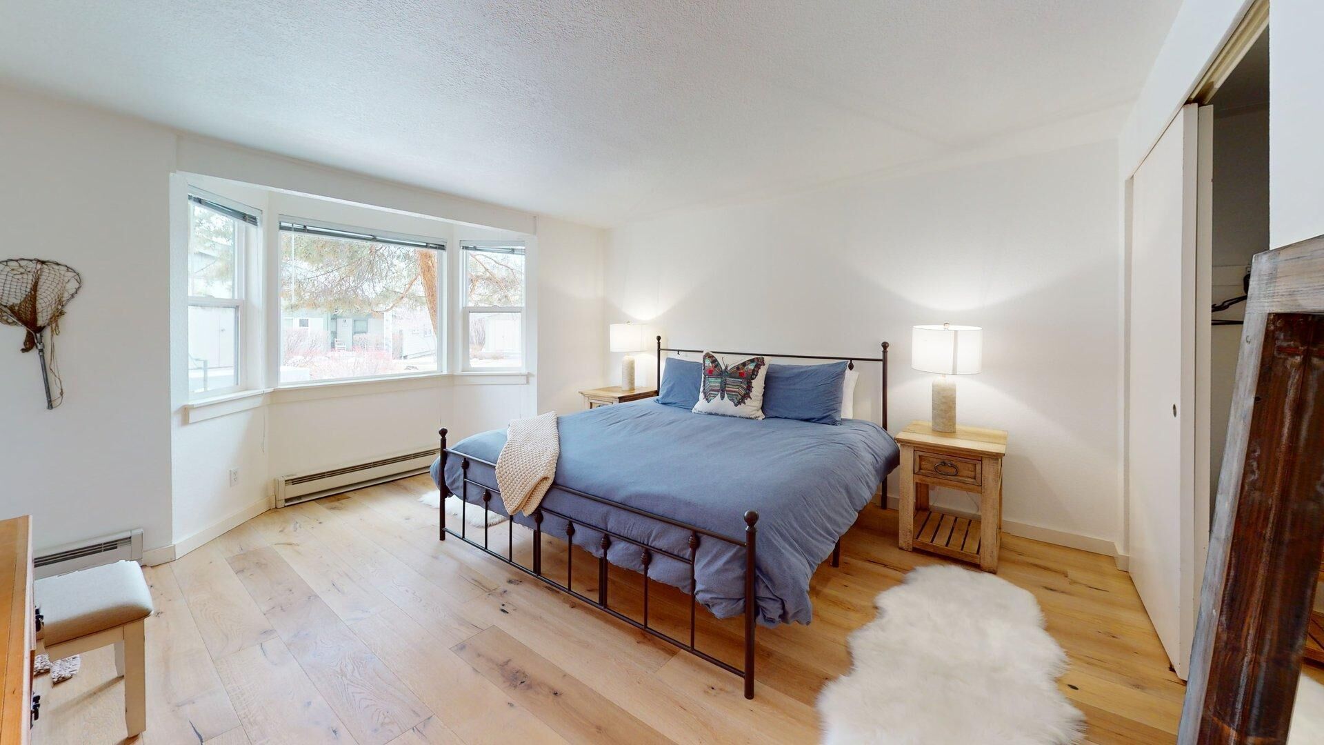 A bedroom with a bed, two bedside tables with lamps, a window, and a door.