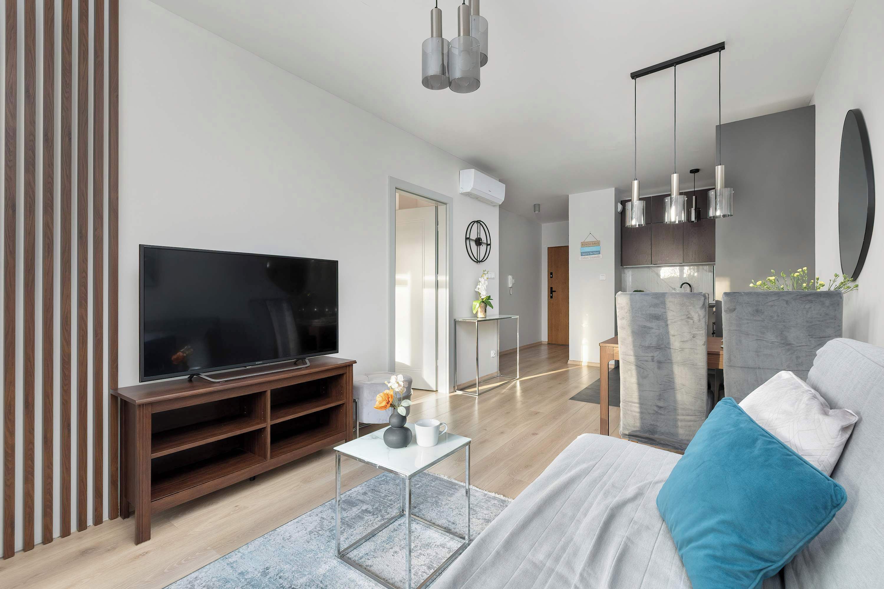 A modern living room with a flat-screen TV, wooden entertainment unit, and a sofa with a blue pillow.