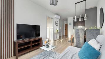 A modern living room with a flat-screen TV, wooden entertainment unit, and a sofa with a blue pillow.