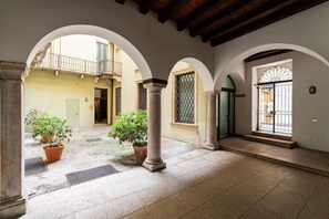 An interior courtyard with arches, columns, potted plants, and a tiled floor. - Cozy penthouse in the heart of Via Mazzini (Verona)