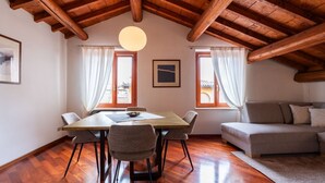 Ein Zimmer mit Holzboden, einem Esstisch mit Stühlen, einer Couch und zwei mit Vorhängen versehenen Fenstern.