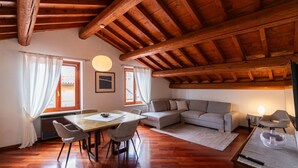 Ein geräumiges Zimmer mit Holzbalkendecke, einem Esstisch mit Stühlen, einem Sofa und einem kleinen Tisch mit Lampe.