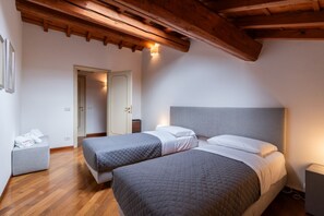 Un dormitorio con dos camas, vigas de madera en el techo, una mesita de noche y una puerta que da a otra habitación.