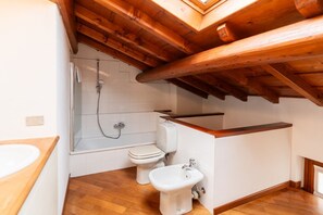 A bathroom with a shower, toilet, bidet, and wooden ceiling beams. - Cozy penthouse in the heart of via Mazzini (Verona)