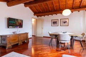 A room with a wooden ceiling, a dining table with chairs, a cabinet, and a television on the wall. - Cozy penthouse in the heart of Via Mazzini (Verona)