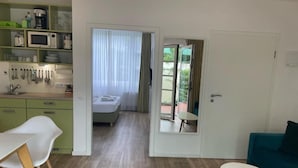 A modern kitchen with a microwave, coffee maker, and utensils on shelves, a dining area with a table and chairs, a bedroom with a bed and curtains, and a sliding glass door leading to an outdoor area. - The Loft (Münster)