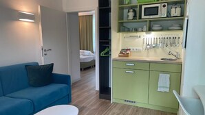Un espace de vie compact comprenant un coin cuisine, un canapé, une petite table et un lit à l’arrière-plan.