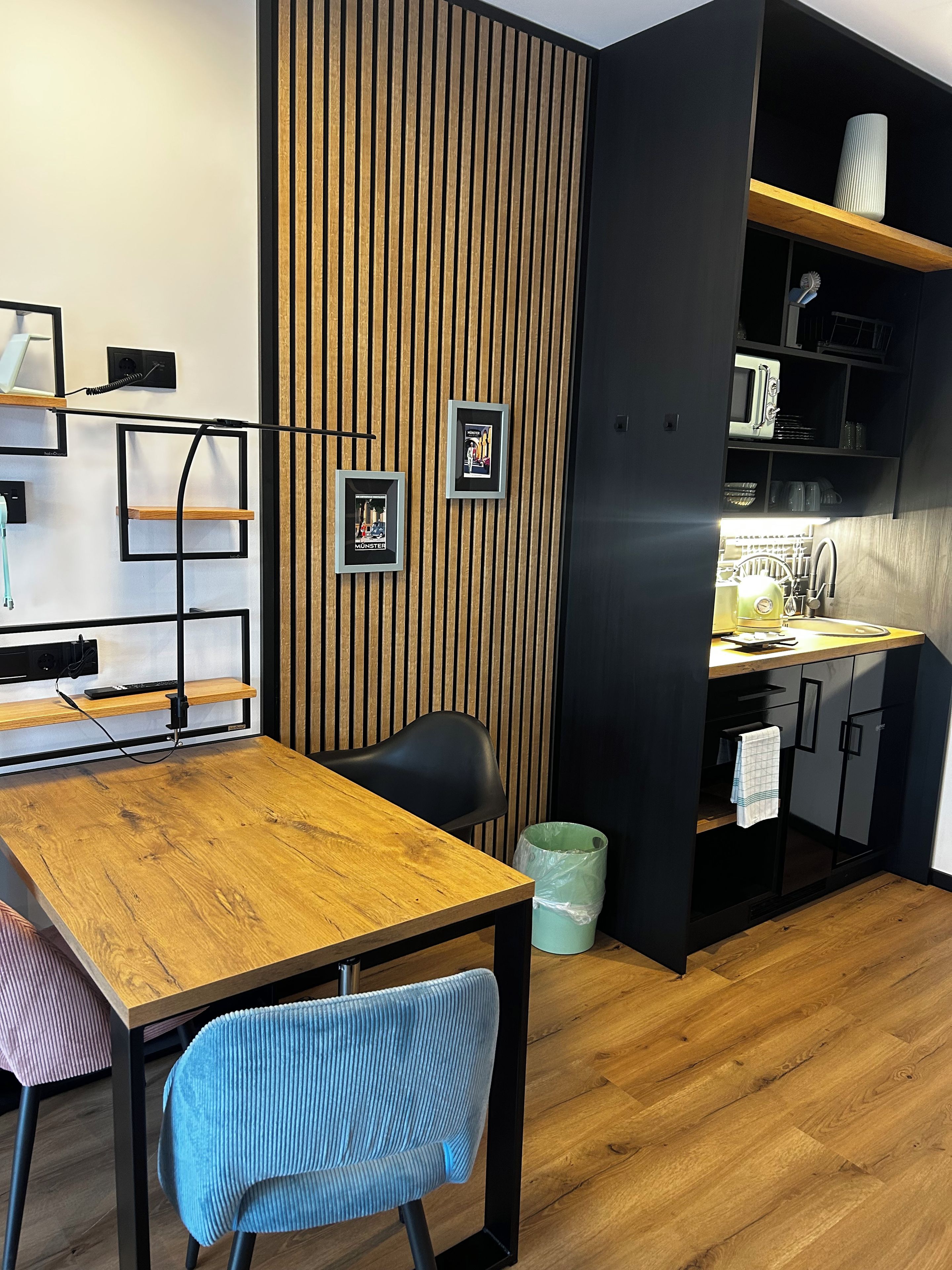 A modern kitchen with a wooden panel wall, a dining table with chairs, and a built-in microwave shelf.