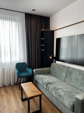 Un salon moderne avec un canapé gris, un fauteuil turquoise, une table basse en bois, un téléviseur à écran plat fixé au mur et un meuble noir pour appareils multimédias.