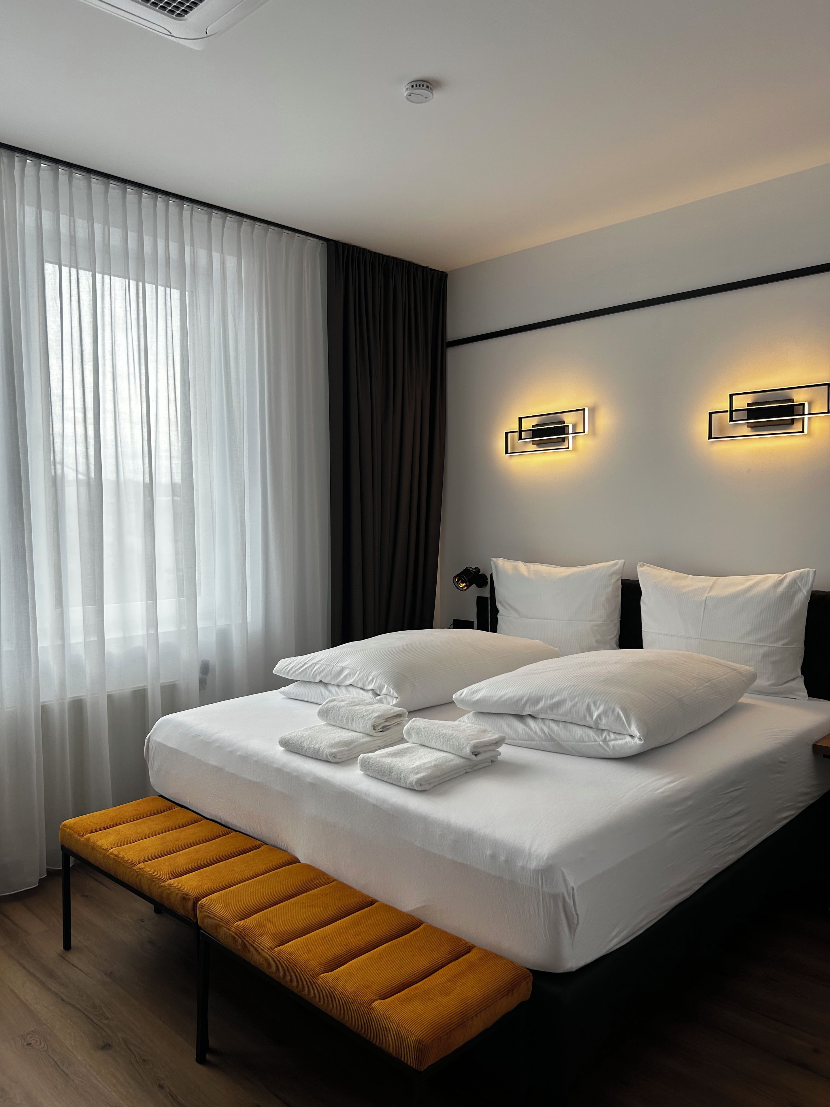 Ein modernes Hotelzimmer mit einem großen Bett, einer Bank und zwei Wandleuchten.