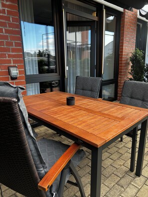 An outdoor patio with a wooden table and chairs, a brick wall, and a glass door. - The Loft (Münster)