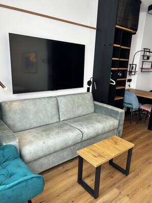 A modern living room with a grey sofa, a wooden coffee table, and a large flat-screen TV mounted on the wall. - The Loft (Münster)