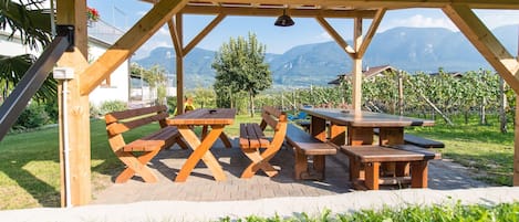 Un pavillon en bois installé à l’extérieur, doté de tables de pique-nique et de bancs, entouré d’une pelouse et offrant une vue sur les montagnes.