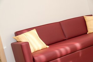 A red leather sofa with two cushions against a plain wall. - 743A Apartments Rogginer | Lagrein (Termeno sulla strada del vino)