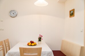 A dining area with a table set for two, a clock on the wall, and a small potted plant. - 743B Apartments Rogginer | Gewürztraminer (Termeno sulla strada del vino)