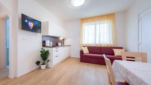 Ein kompakter Wohnbereich mit Küchenzeile, einem roten Sofa, einem Esstisch und einem an der Wand befestigten Fernseher.