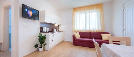 A compact living space with a kitchenette, a red sofa, a dining table, and a television mounted on the wall.