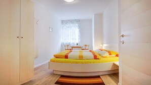 Ein Schlafzimmer mit Bett, Fenster, Sessel und Nachttisch.
